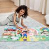 0000772504164-5 A young child sits on a rug and assembles the Melissa & Doug Ms. Rachel Floor Puzzle Farm, featuring colorful farm animals, a barn, and a rainbow.