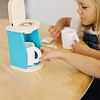 A little girl is playing with a Melissa & Doug Brew and Serve Wooden Coffee Maker Set.