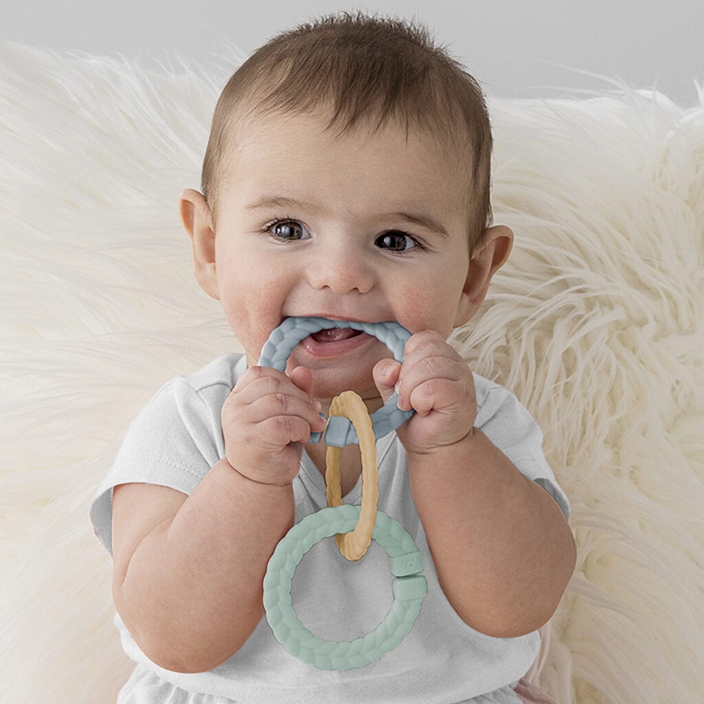 A baby is chewing on an Itzy Ritzy Teething Baby Gift Set.