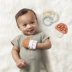 A baby is laying on a blanket with an Itzy Ritzy Teething Baby Gift Set and teether.