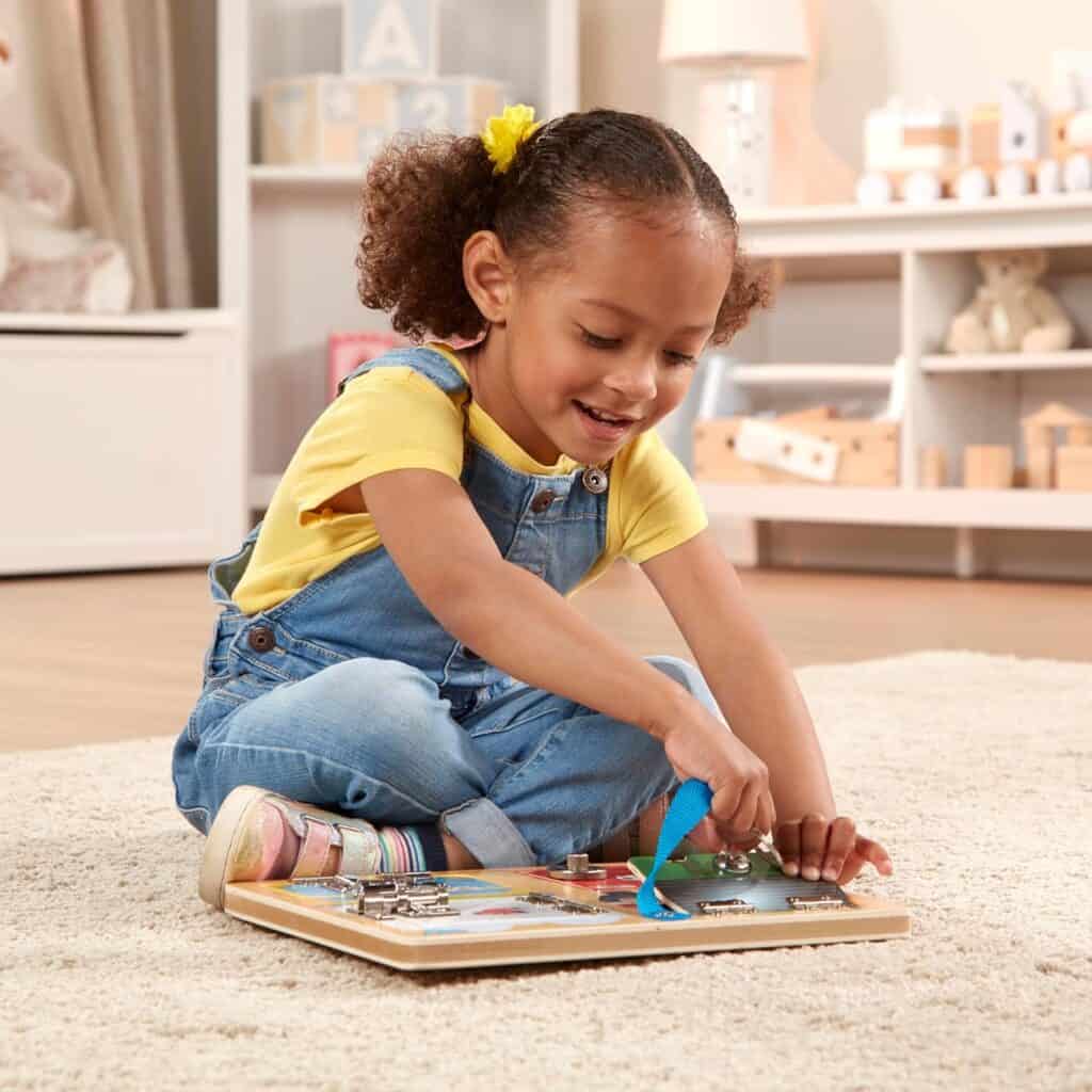 A little girl playing with a Melissa & Doug Locks and Latches Board on the floor.