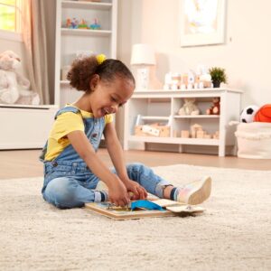 A little girl sitting on the floor playing with a Melissa & Doug Locks and Latches Board.