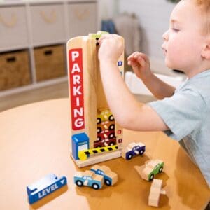 A young boy playing with a Melissa & Doug Stack & Count Wooden Parking Garage With 10 Cars at a table.