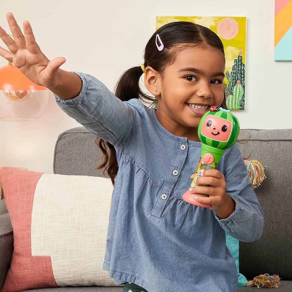 A little girl is waving a First Act CoComelon Musical Sing-Along Microphone Plays Clips ‘Thank You’ Song Clip in the air.