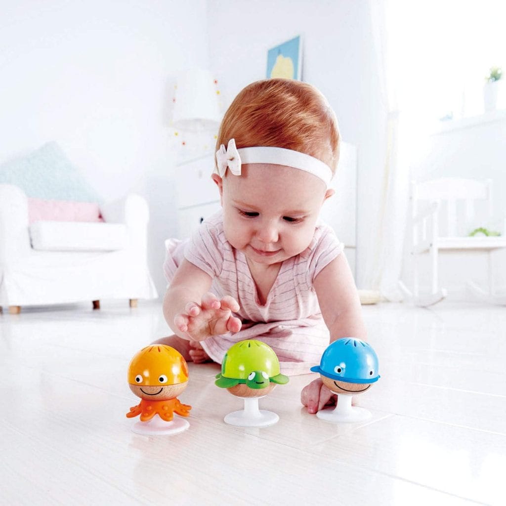 A baby is playing with the Hape Put-Stay Sea Animal Suction Rattle Set Three Toys on the floor.