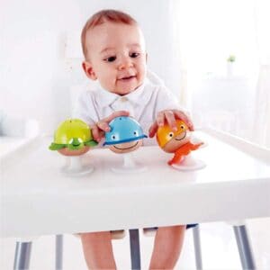 A baby in a high chair playing with the Hape Put-Stay Sea Animal Suction Rattle Set Three Toys.