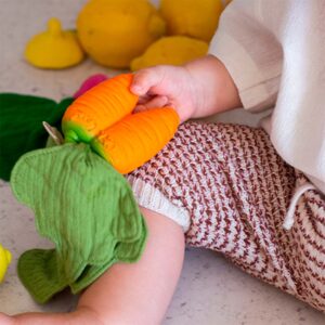 A baby is playing with Oli & Carol Cathy the Carrot Mini Doudou Teether Natural Rubber and lemons.