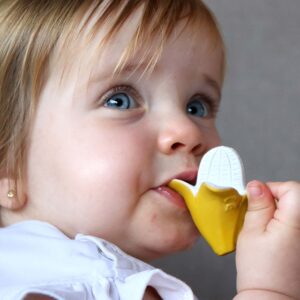 A little girl is chewing on an Oli & Carol Anita the Bananita Mini Baby Teether Natural Rubber.