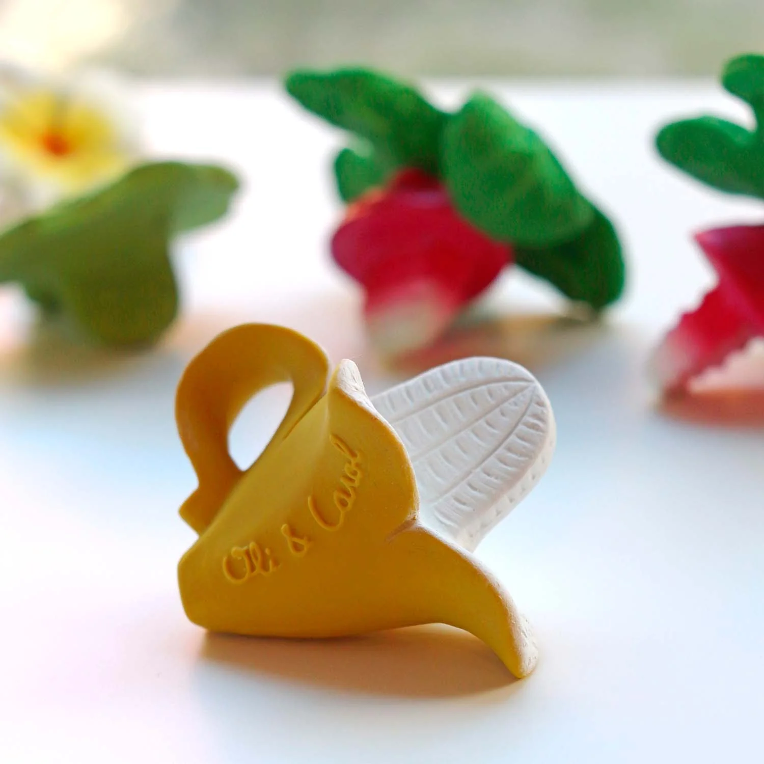 Oli & Carol Anita the Bananita Mini Baby Teether Natural Rubber (2) A Oli & Carol Anita the Bananita Mini Baby Teether Natural Rubber and flowers on a table.