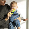 A woman holding a baby while holding an Oli & Carol Corn Rattle Toy Teether Baby Natural Rubber.