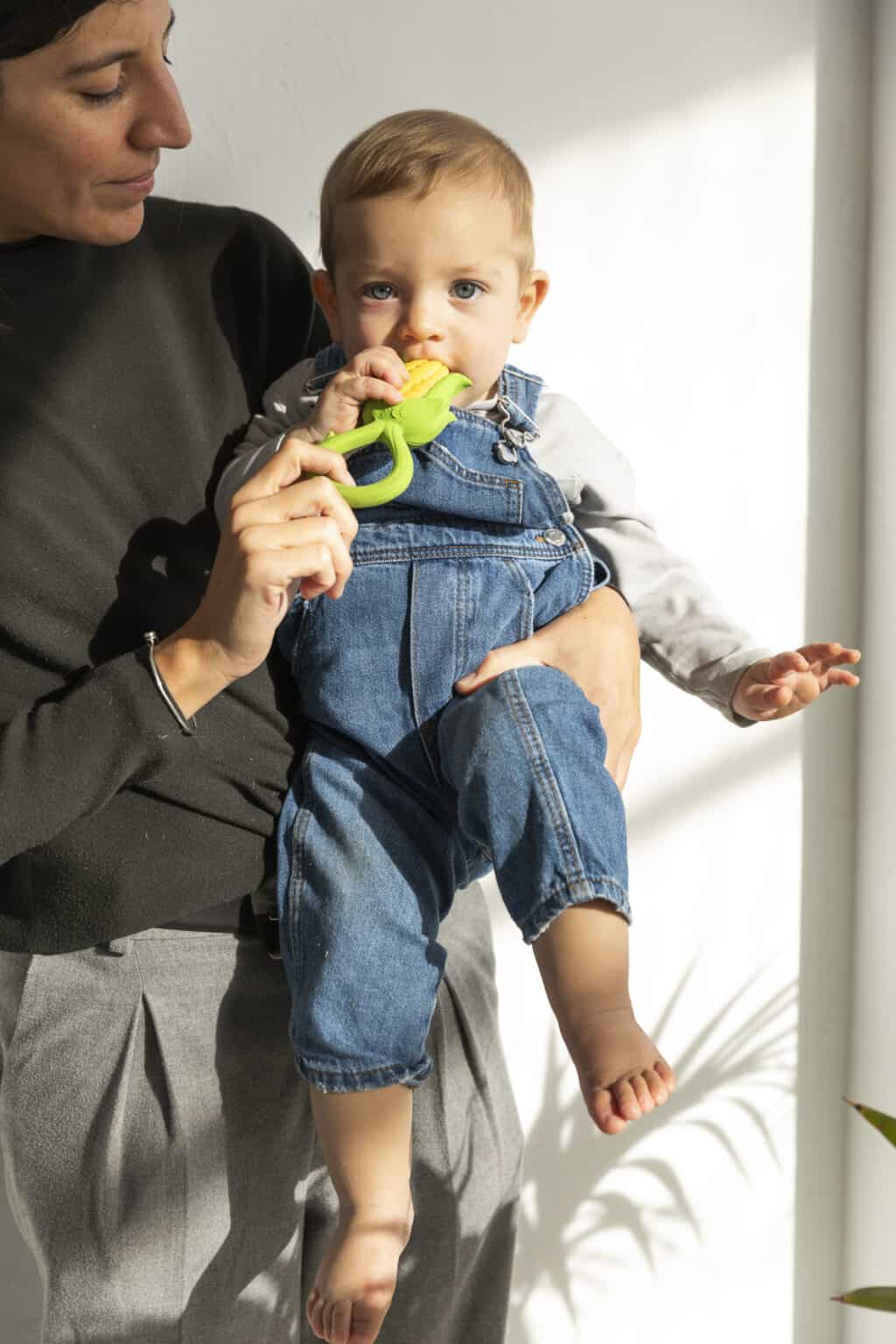 A woman holding a baby while holding an Oli & Carol Corn Rattle Toy Teether Baby Natural Rubber.