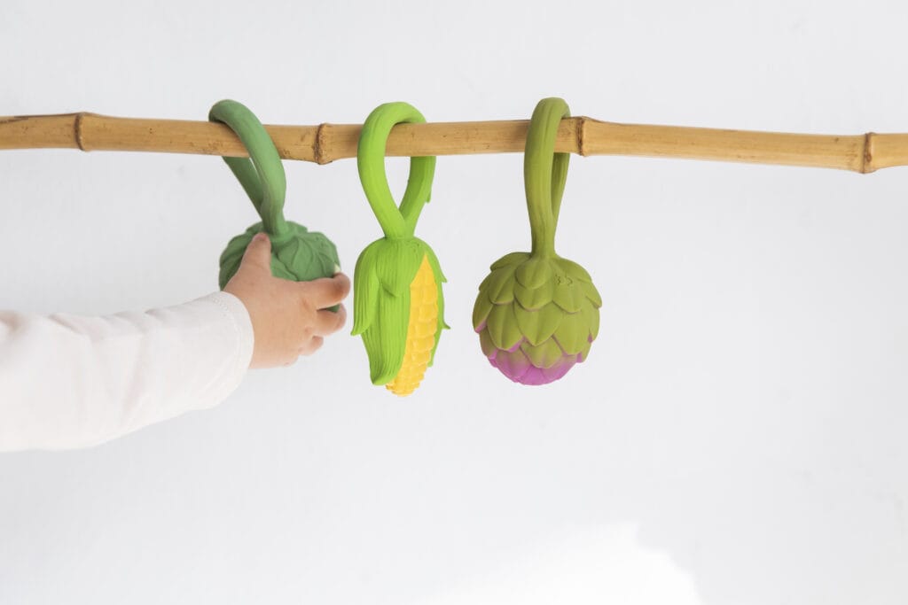 A child is holding an Oli & Carol Corn Rattle Toy Teether Baby Natural Rubber on a bamboo branch.