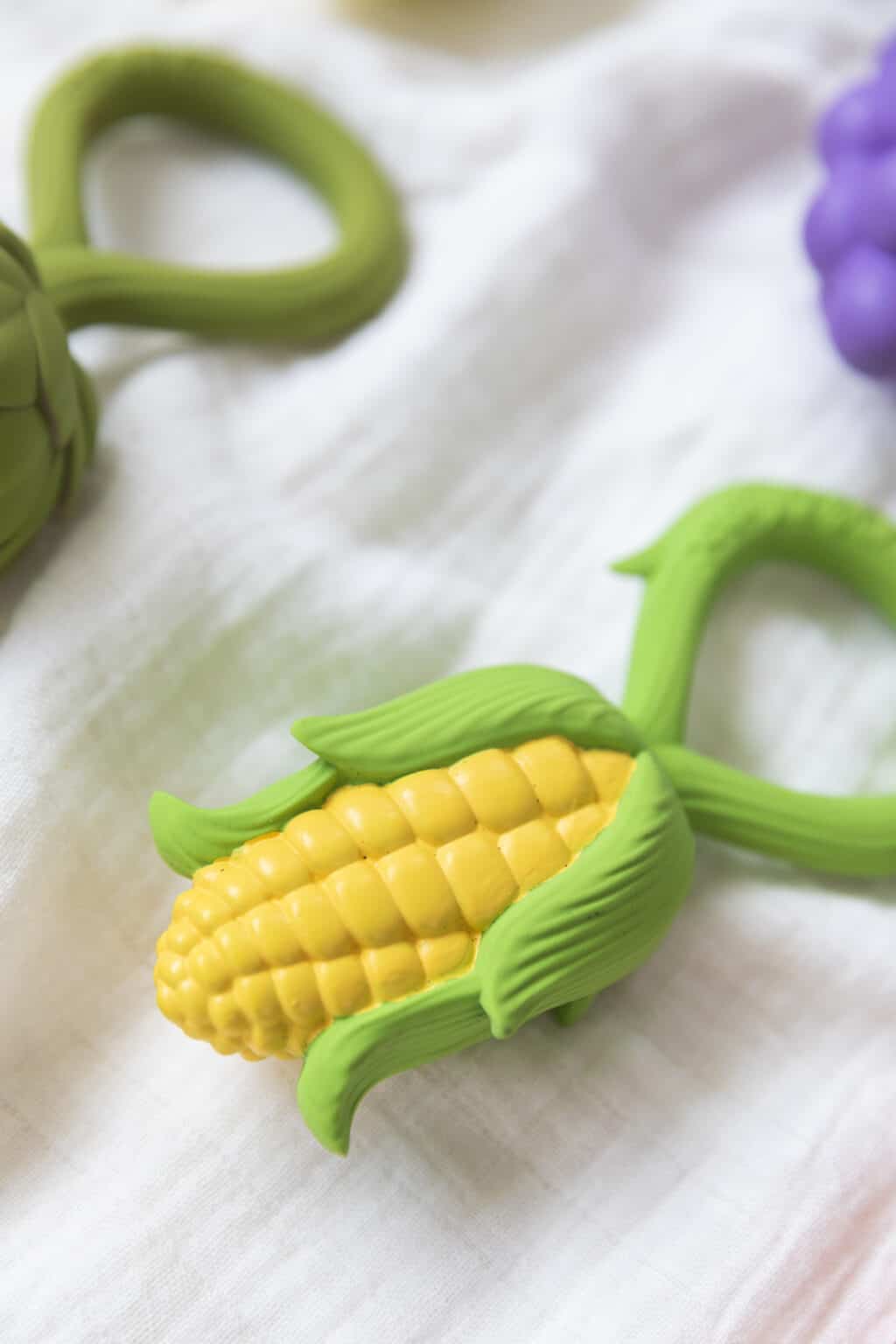 A set of Oli & Carol Corn Rattle Toy Teethers on a white cloth.