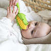 A baby is chewing on an Oli & Carol Corn Rattle Toy Teether Baby Natural Rubber in a basket.