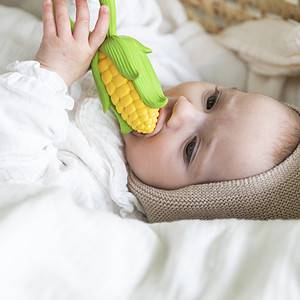 A baby is chewing on an Oli & Carol Corn Rattle Toy Teether Baby Natural Rubber in a basket.