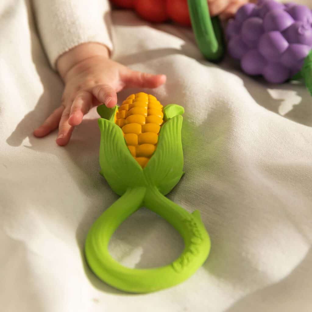 A baby is holding an Oli & Carol Corn Rattle Toy Teether Baby Natural Rubber.