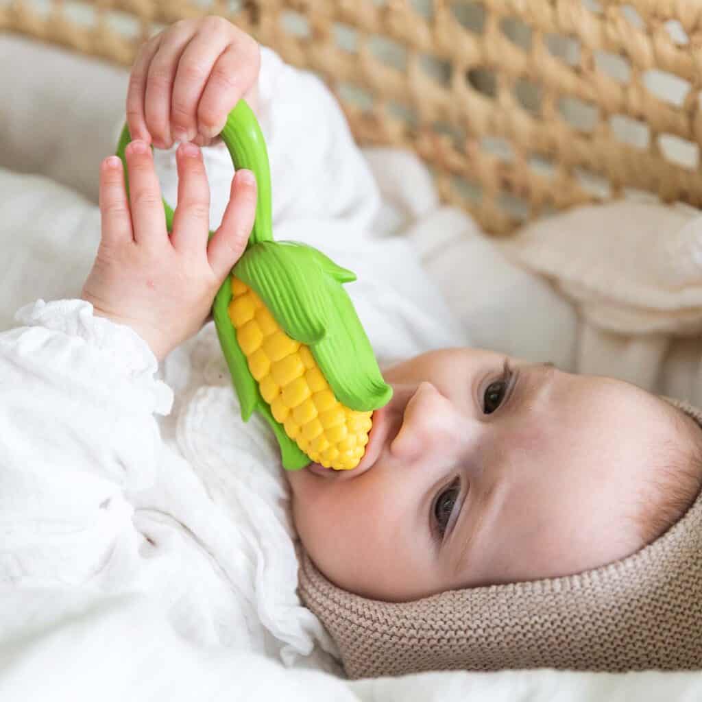 A baby is chewing on an Oli & Carol Corn Rattle Toy Teether Baby Natural Rubber.
