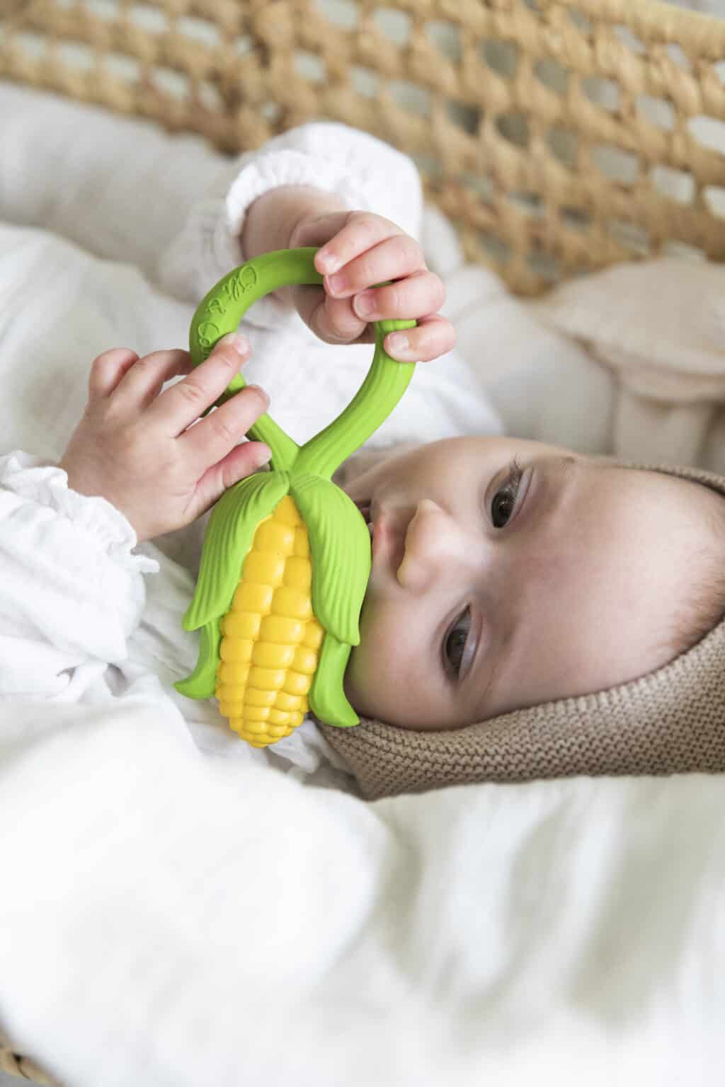 A baby is playing with an Oli & Carol Corn Rattle Toy Teether Baby Natural Rubber in a basket.