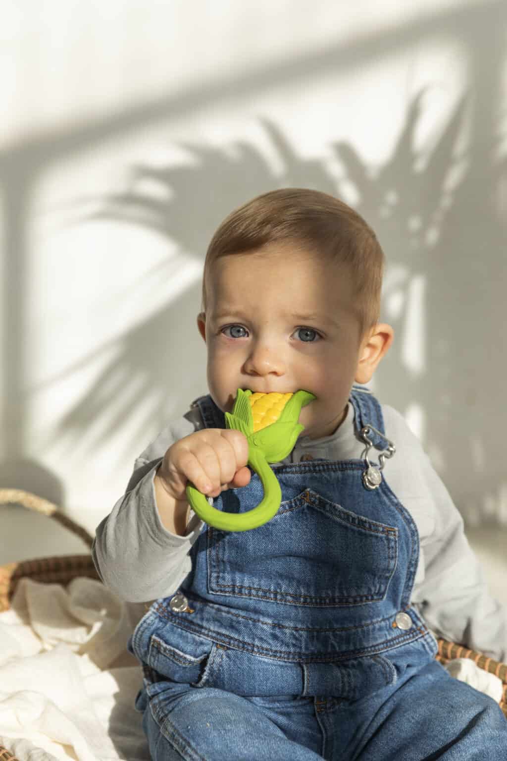 A baby is sitting in a basket with an Oli & Carol Corn Rattle Toy Teether Baby Natural Rubber.