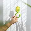 A person holding an Oli & Carol Corn Rattle Toy Teether Baby Natural Rubber in front of a window.