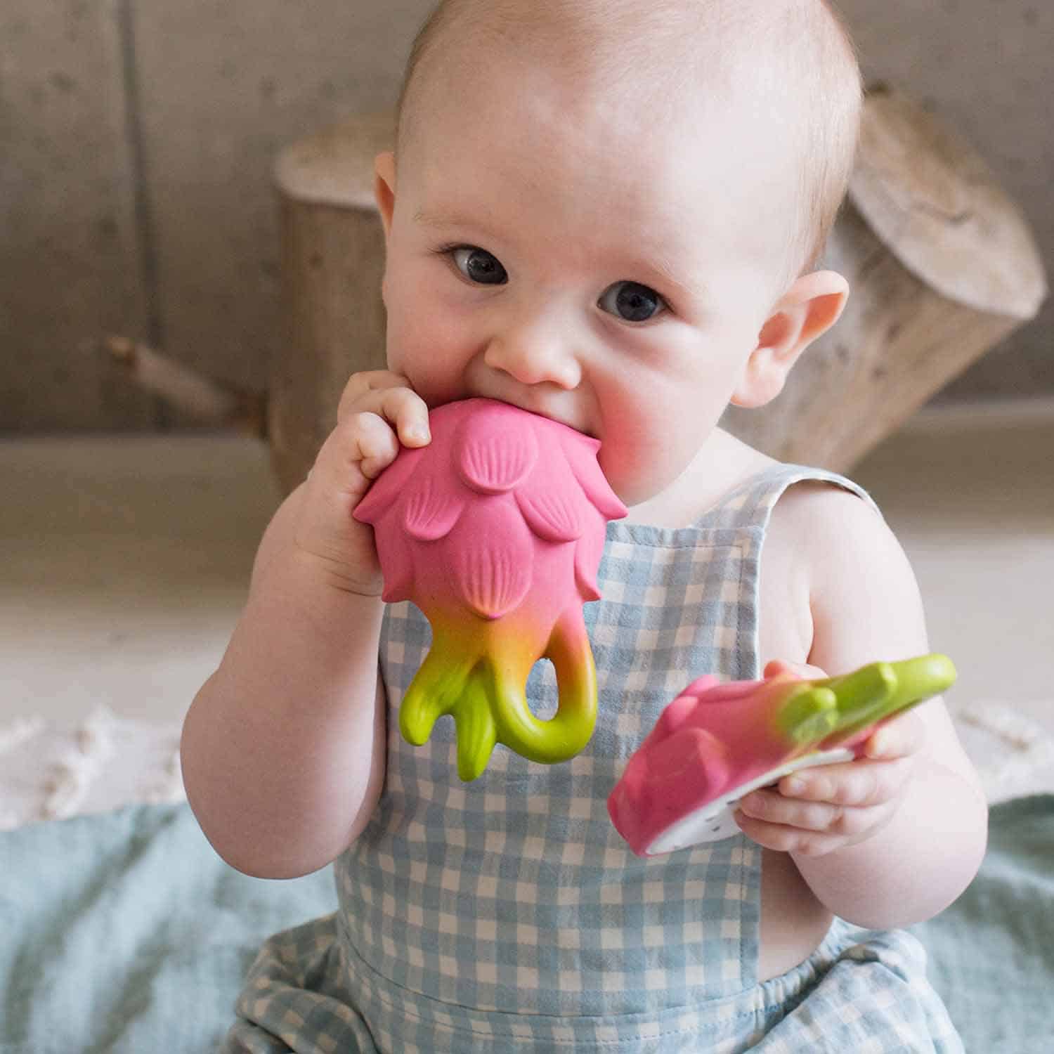 Oli & Carol Fucsia de Dragonfruit Baby Teether Natural Rubber (1) A baby is chewing on an Oli & Carol Fucsia de Dragonfruit Baby Teether Natural Rubber.