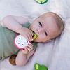 A baby is laying on a blanket with the Oli & Carol Fucsia de Dragonfruit Baby Teether Natural Rubber.
