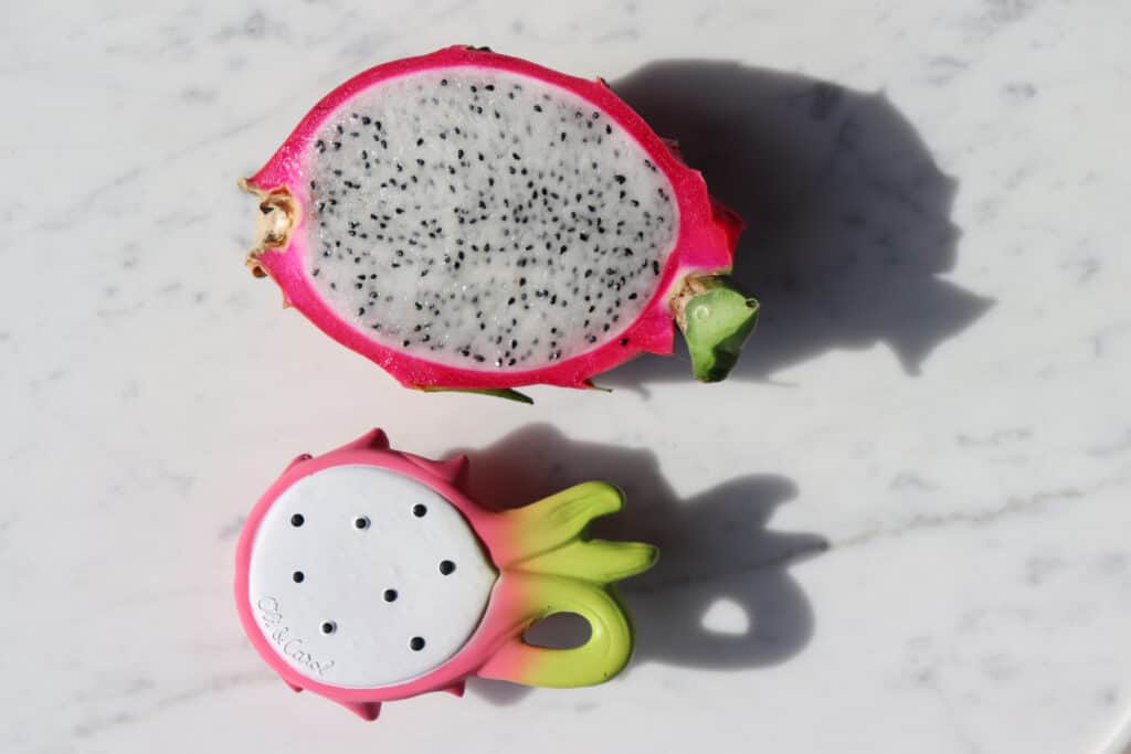 An Oli & Carol Fucsia de Dragonfruit Baby Teether Natural Rubber is sitting on top of a marble table.