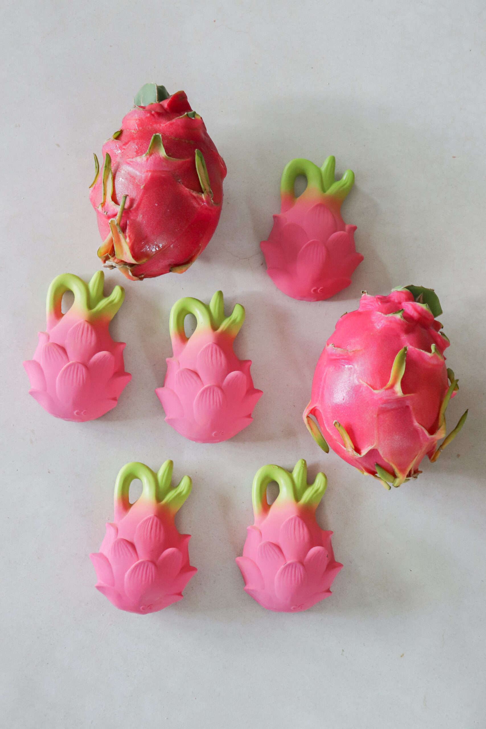 Oli & Carol Fucsia de Dragonfruit Baby Teether Natural Rubber (6) A group of Oli & Carol Fucsia de Dragonfruit Baby Teether Natural Rubber decorations on a white surface.