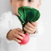 A baby is holding the Oli & Carol Ramona the Radish Baby Teether Natural Rubber.