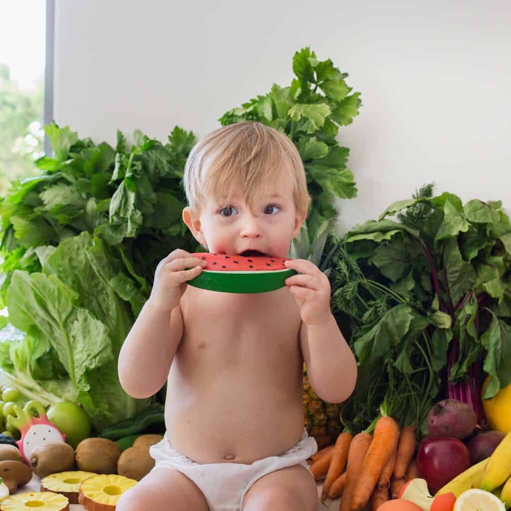 A baby is eating the Oli & Carol Wally the Watermelon Baby Teether Natural Rubber.