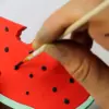 A hand painting the Oli & Carol Wally the Watermelon Baby Teether Natural Rubber.