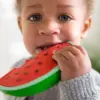 A baby is eating an Oli & Carol Wally the Watermelon Baby Teether Natural Rubber toy.