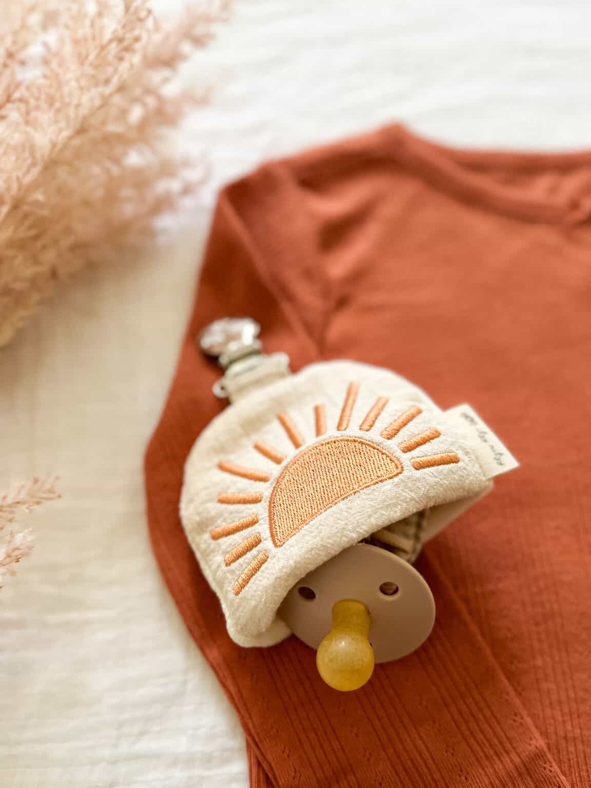 An Itzy Ritzy Soothe & Store Pacifier Clip & Storage Pouch with a sun on it.