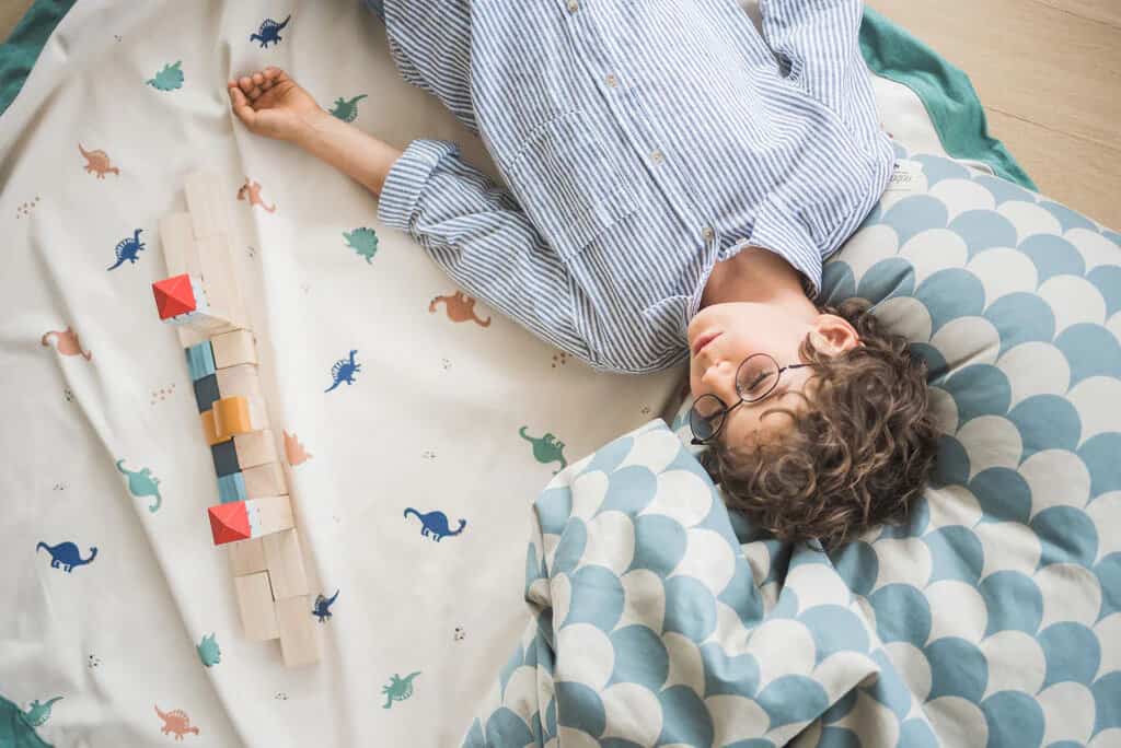 A young boy laying on a bed with a toy on it.