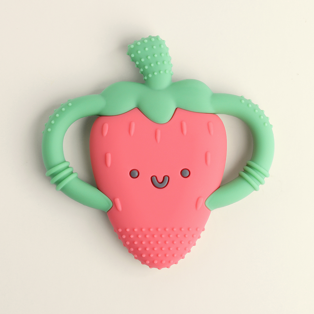 The Itzy Ritzy Chew Crew Silicone Teether with Handles is a strawberry-shaped baby teether featuring a smiling face and two green handles designed for easy gripping.