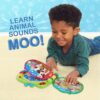 cocomelon-learningbook-103 A young boy lies on a carpet, smiling as he plays with the CoComelon Learning Book Interactive Toy. The text on the wall reads “LEARN ANIMAL SOUNDS MOO!” against a blue patterned background with playful icons.