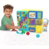 cocomelon-learningkitchen-74 A young child plays with the CoComelon Learning Kitchen 34 Piece Interactive Play Kitchen, which features alphabet buttons, toy food items, and a chef cutout on a white surface.