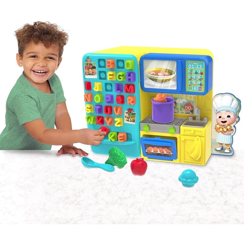 cocomelon-learningkitchen-74 A young child plays with the CoComelon Learning Kitchen 34 Piece Interactive Play Kitchen, which features alphabet buttons, toy food items, and a chef cutout on a white surface.