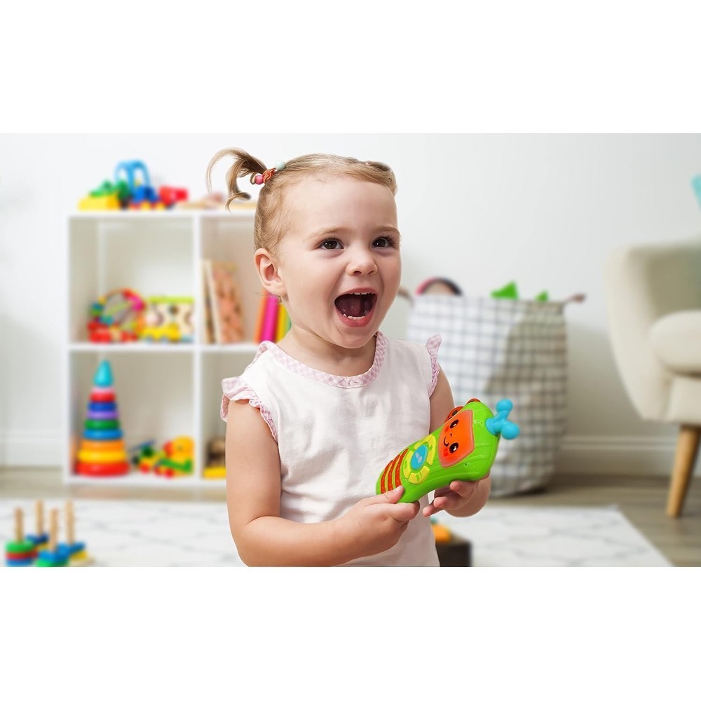 cocomelon-singingremote-71 A young child with pigtails smiles and holds the CoComelon Learn and Play Singing Remote Toddler Musical Toy Microphone, surrounded by shelves and toys in a cheerful playroom.