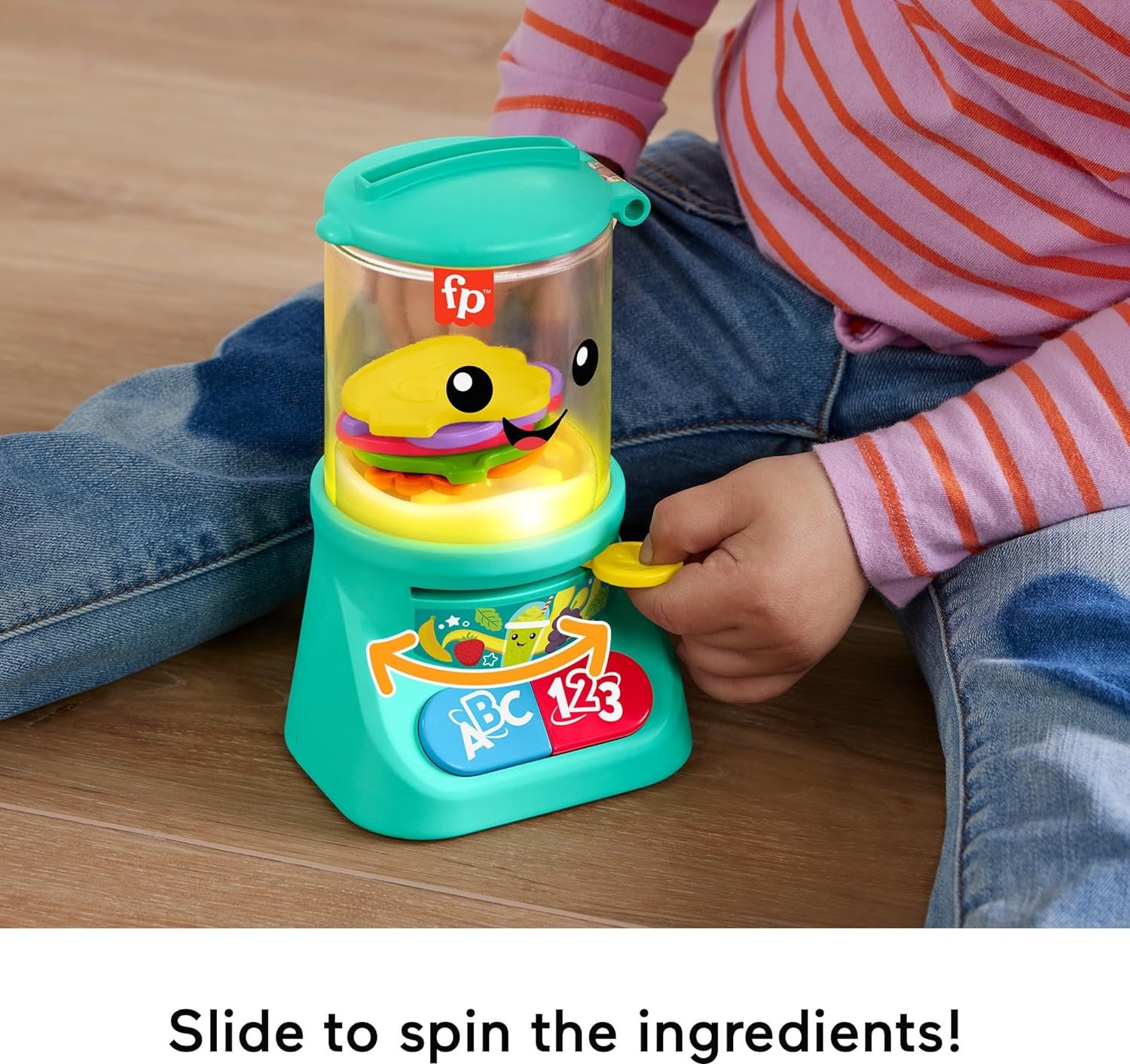 fisher-price-laugh-learn-counting-colors-smoothie-makers (6) A child is playing with a Fisher-Price Laugh & Learn Baby & Toddler Toy Counting & Colors. The toy has a transparent top, a smiling face graphic, and labeled buttons on the front. The child is wearing blue jeans and a red-striped shirt.