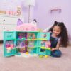gabbydollhouse-mercatsparoom-86 A young girl smiles as she plays with the Gabby’s Dollhouse MerCat’s Spa Room Playset, which features a colorful, multi-story dollhouse with cat ears and includes several small dolls like the MerCat figure along with surprise toy furniture inspired by the Netflix series. She holds a doll in her right hand while enjoying the imaginative play set.