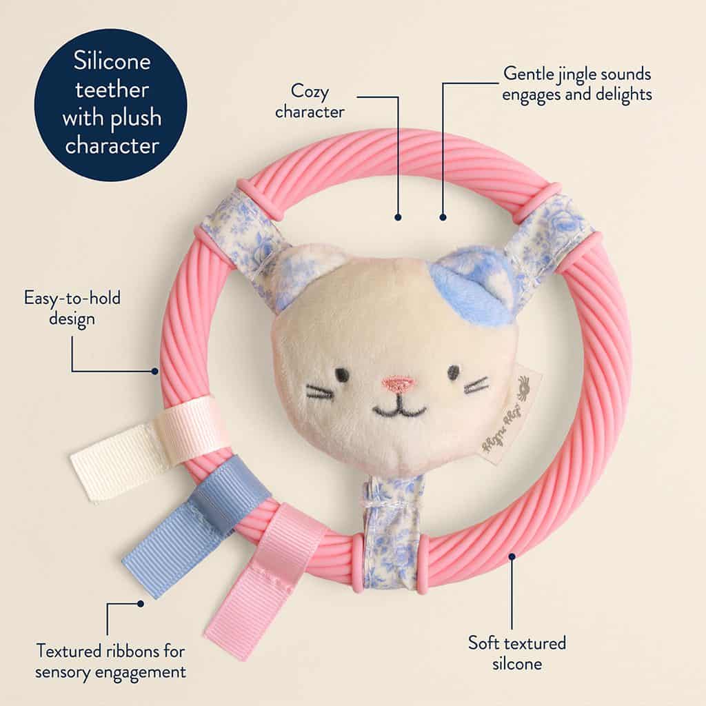 itzy-ring-pal-kitty-03 Pink silicone teether ring with a soft plush animal face, textured ribbons, fabric tabs, and a gentle jingle sound; labeled features highlight sensory and design elements.