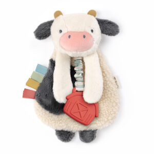 A plush cow toy with a black and white body, floppy ears, a pink nose, and a red barn-shaped teether attached. The toy also features colorful ribbon tags on one side.