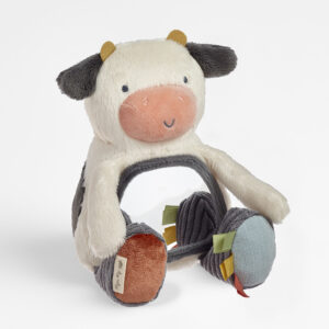Plush toy shaped like a cow with a round central opening, black and white fur, black ears, orange nose, and multicolored ribbons on the feet.