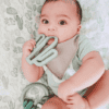 A baby is laying on a bed with a cactus toy.