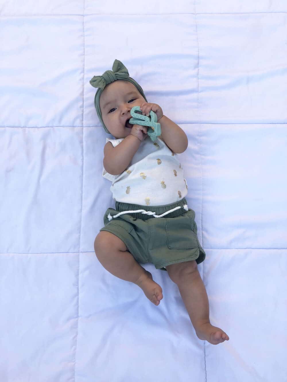 A baby laying on a bed with a toy in her mouth.