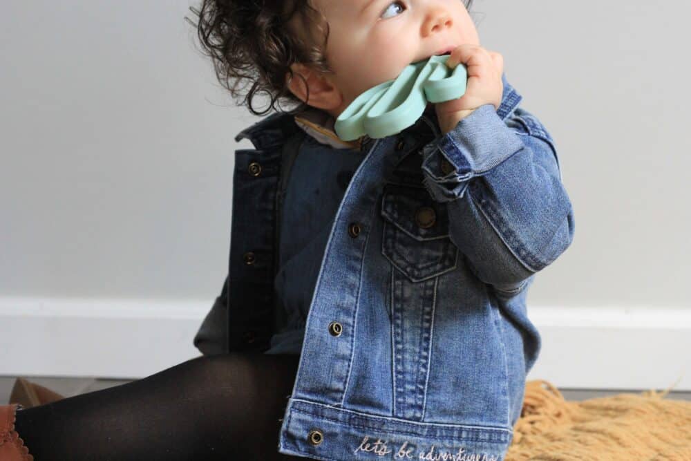 A baby wearing a denim jacket sitting on a rug.