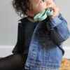 A baby wearing a denim jacket sitting on a rug.