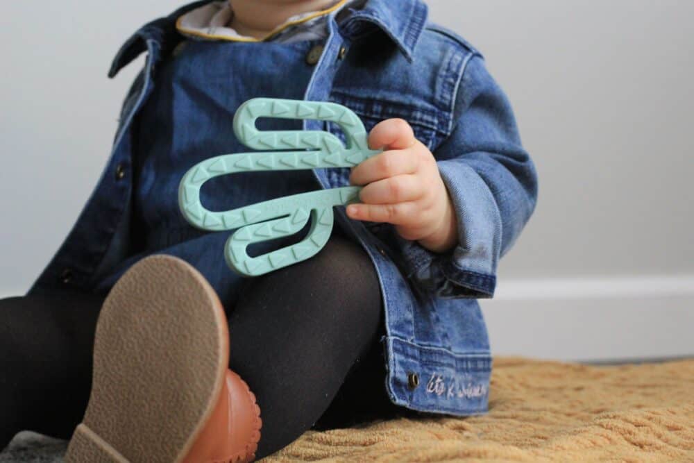 A baby is sitting on a rug with a green cactus toy.