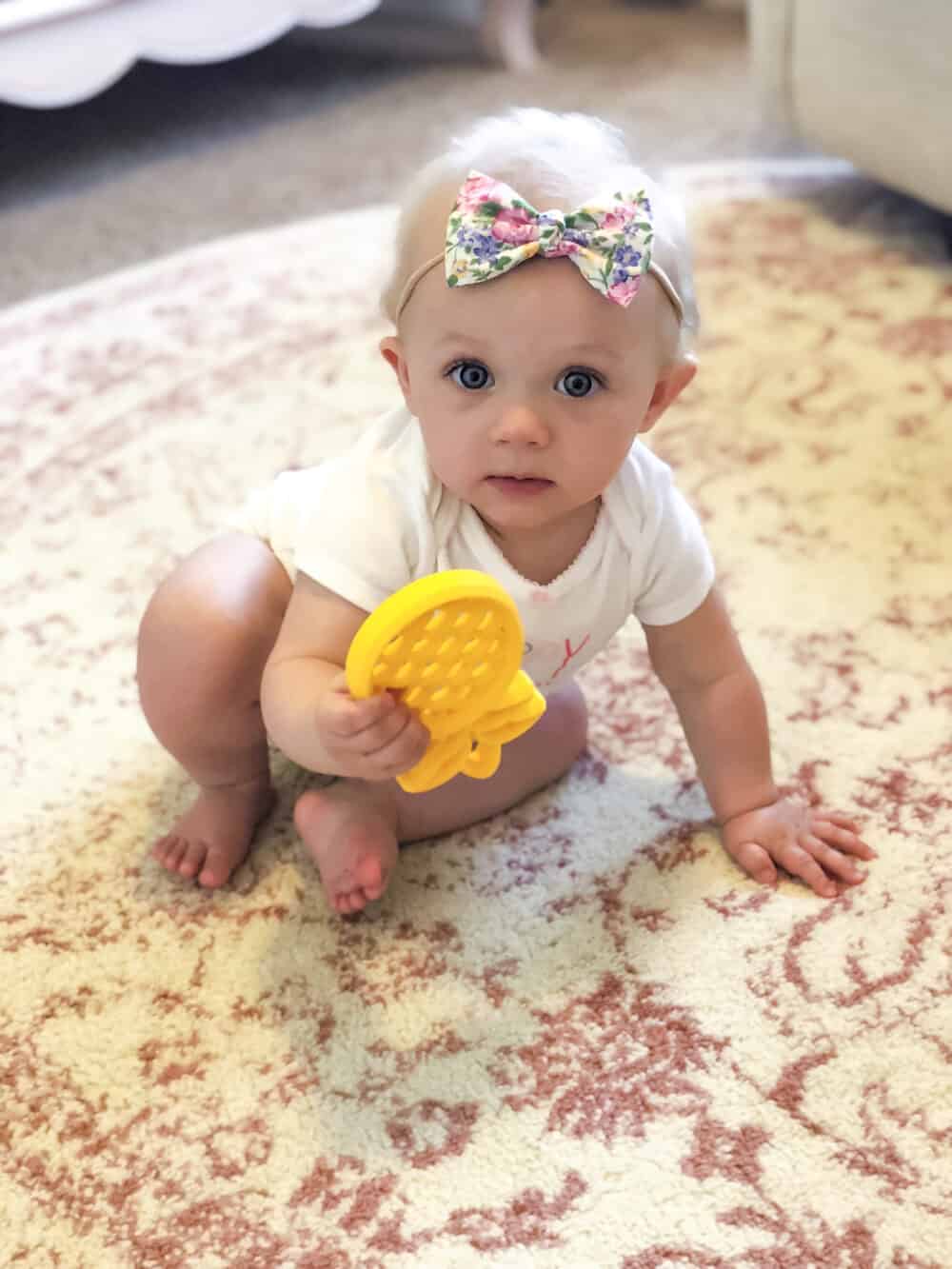 A baby playing with a yellow toy on a rug.